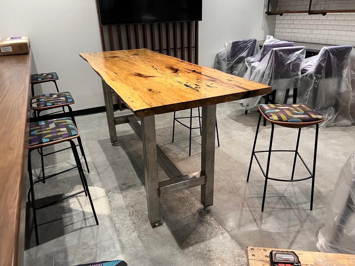Thick natural-edge wood tabletop on a rectangular metal base, surrounded by stools.